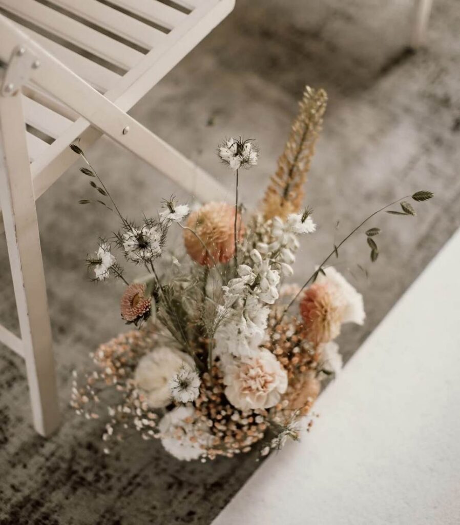 Blumendekoration in Apricot und Weiß neben einem Traustuhl